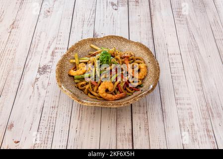 Ciotola di tagliatelle di udon fritte con gamberetti e verdure su tavola di legno Foto Stock