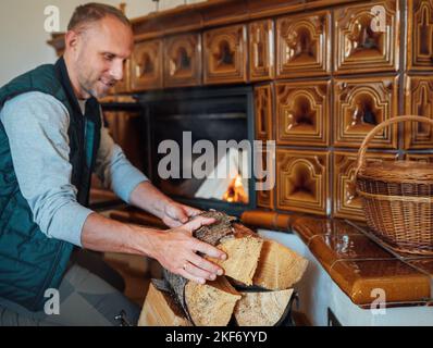 Uomo sorridente che mette i tronchi di legno nel mantel casa Fire.Home dolce casa e inverno vacanze campagna concept immagine Foto Stock