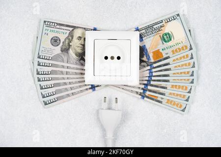 Presa bianca con spina con molte banconote da 100 dollari su sfondo chiaro. Concetto di aumento dei prezzi dell'elettricità nel mondo. Alta energia c Foto Stock
