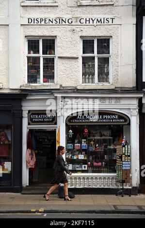 Donna cammina davanti a un vintage o vecchio Shopfront un ex dispensatore chimico ora un negozio di telefonia mobile Stratford-upon-Avon Inghilterra Foto Stock