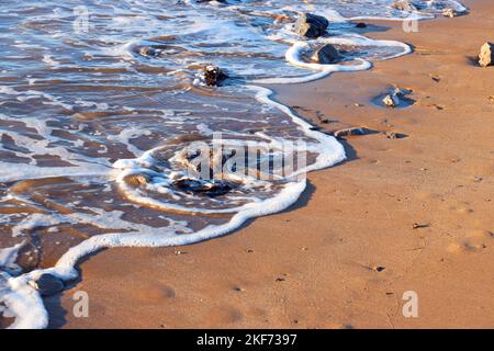 Schiuma della marea in arrivo sulla spiaggia di sabbia. Foto Stock