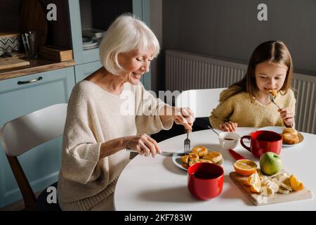 Donna anziana felice che fa colazione con sua nipote in cucina a casa Foto Stock
