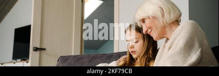 Ragazza bianca e sua nonna abbracciando e collocando sul divano insieme a casa Foto Stock