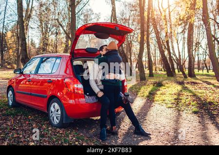 Felice coppia amorevole rilassarsi in tronco auto abbracciando nella foresta autunnale. Uomo e donna viaggiano in auto. Foto Stock