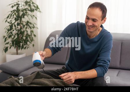 man rimuove le pillole di tessuto utilizzando un rasoio per pelucchi. Foto Stock