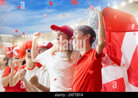 Tifoso di calcio danese allo stadio. Tifosi danesi sul campo di calcio che guardano la squadra. Gruppo di sostenitori con bandiera e maglia nazionale Foto Stock