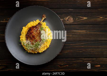 Gamba d'anatra con risotto, zucca ed erbe su fondo scuro Foto Stock