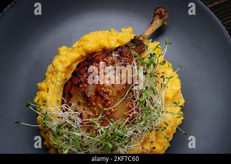 Gamba d'anatra con risotto, zucca ed erbe su fondo scuro Foto Stock