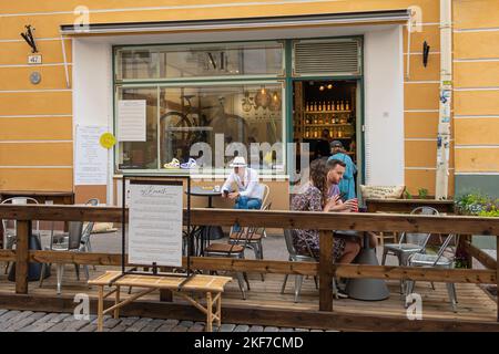 Estonia, Tallinn - 21 luglio 2022: Vista frontale della caffetteria 5Senses al Pikk 47, facciata gialla. Persone ai tavoli all'esterno e all'interno. I vestiti aggiungono i colori Foto Stock
