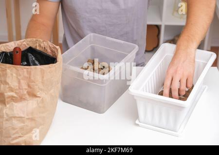 Un uomo si addormenta in una scatola di fiori di argilla espansa. Sporchi preparazione, il primo strato espanse creta. Preparazione per piantare piante. Giardinaggio a casa. Foto Stock