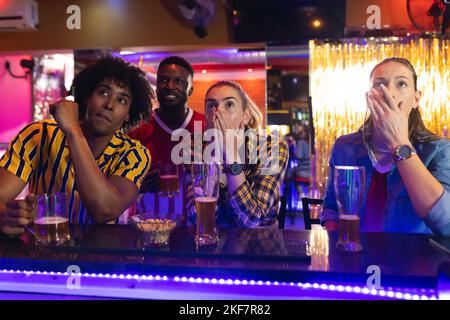 Quattro amici maschi e femmine, diversi e tesi, che guardano una partita di sport in un bar Foto Stock