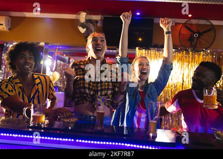 Gruppo di amici maschi e femmine entusiasti che guardano una partita sportiva in un bar, festeggiando Foto Stock