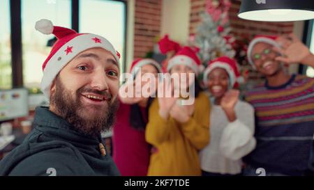 Diverse persone scattano foto vicino all'albero di natale in ufficio decorate con ornamenti stagionali. Registrare video e scattare foto per divertirsi, festeggiando la festa delle vacanze invernali. Foto Stock