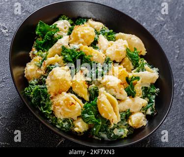 porzione di pasta cotta al forno con balena verde ricoperta di croccante pangrattato in una ciotola nera su un tavolo di cemento, primo piano Foto Stock