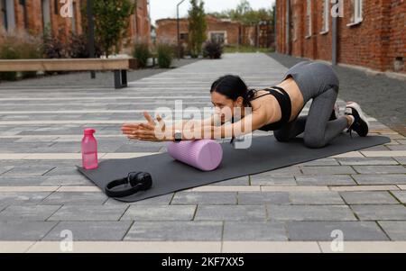 Donna fitness che fa esercizi con un rullo di massaggio sulla strada Foto Stock