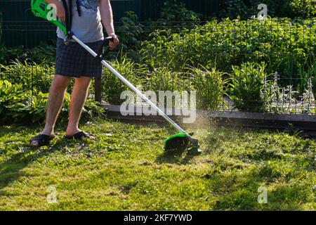 Defocalizzazione del tagliaerba. Un uomo che falciava l'erba. Vista all'aperto di un giovane lavoratore che utilizza un rasaerba che taglia l'erba in uno sfondo di natura sfocata Foto Stock