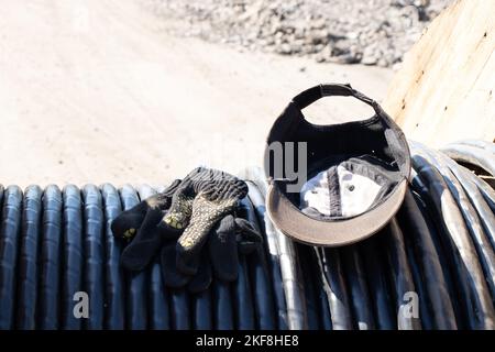 il cappello da baseball e i guanti da costruzione giacciono su un cavo nero lasciato dal costruttore al sole Foto Stock