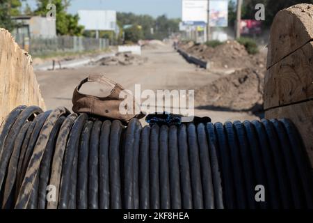 il cappello da baseball e i guanti da costruzione giacciono su un cavo nero lasciato dal costruttore al sole Foto Stock