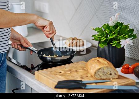 Processo di cottura della donna prima colazione in cucina. Le mani femminili preparano l'omeletta in padella, usando il fornello a induzione Foto Stock