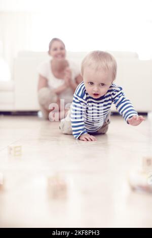 Guarda, hes che striscio. Un ragazzo carino che striscio sul pavimento mentre la sua madre orgogliosa guarda sopra. Foto Stock
