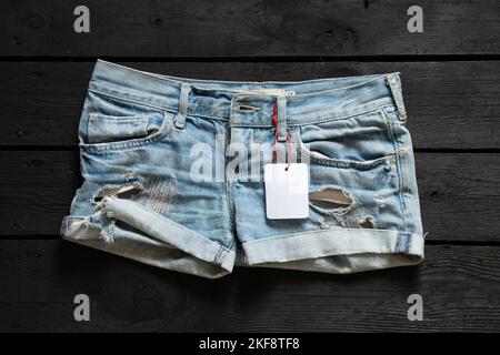 pantaloncini denim donne con cartellino bianco per testo sul tavolo, cartellino per pantaloncini corti, posto per prezzo Foto Stock