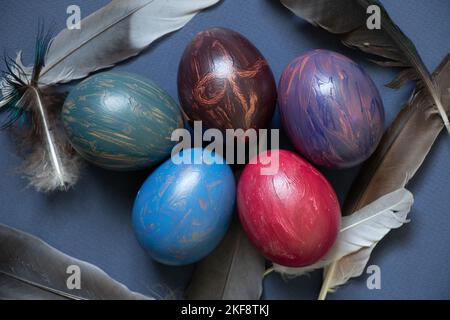 uova di pollo decorate con pitture multicolori acquarelli e piume di colomba su sfondo blu, prazdnik pasquale e cultura Foto Stock