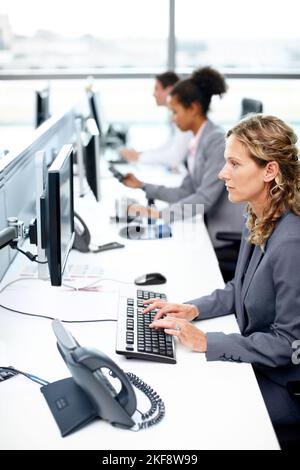 Si concentra sulla realizzazione di un lavoro eccellente. Vista del profilo di una donna d'affari seria che lavora al suo computer con i suoi colleghi in background. Foto Stock