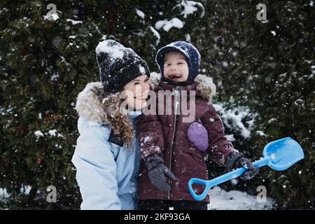 Famiglia felice, madre e figlio che si divertono all'aperto in inverno neve sfondo natura. Mamma e bambino giocano a palla di neve nel parco invernale all'aperto Foto Stock