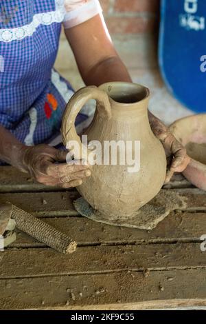 Fare ceramica di argilla rossa. Il vasaio attacca un manico per fare una caraffa a San Marcos Tlapazola, Messico. Indossa un abito tradizionale in raso An Foto Stock