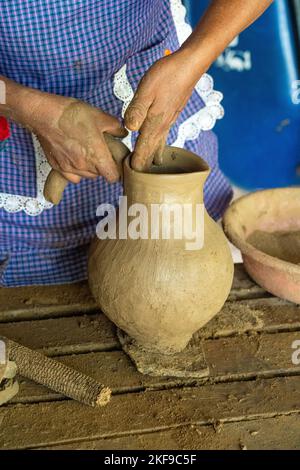 Fare ceramica di argilla rossa. Il vasaio attacca un manico per fare una caraffa a San Marcos Tlapazola, Messico. Indossa un abito tradizionale in raso An Foto Stock