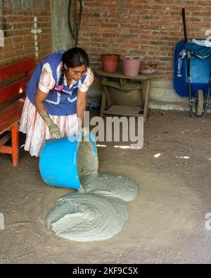 Fare ceramica di argilla rossa. Potter versando fuori l'argilla mescolata su una base di sabbia per asciugare per fare la ceramica di argilla rossa a San Marcos Tlapazola, Messico. È portatrice Foto Stock