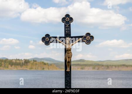 Crocifisso - statua di Gesù Cristo su una croce, sullo sfondo del paesaggio con acqua, colline e cielo blu con le nuvole Foto Stock