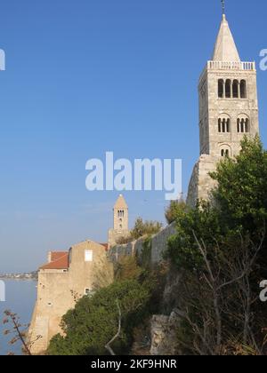 Alti campanili punteggiano lo skyline dell'isola croata di Rab, dove il vecchio quartiere medievale e le mura della città si ergono in cima alle scogliere. Foto Stock