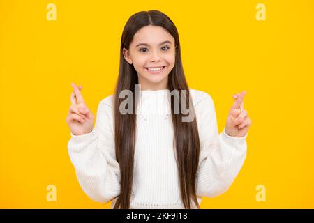 Bambino adolescente che tiene le dita incrociate per Buona fortuna. Teen girl prega e spera che i sogni si avverino, isolato su sfondo giallo. Foto Stock