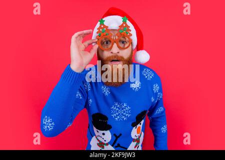 festa di natale. uomo curioso in bicchieri da festa a natale. uomo a festa chirstmas isolato su rosso Foto Stock