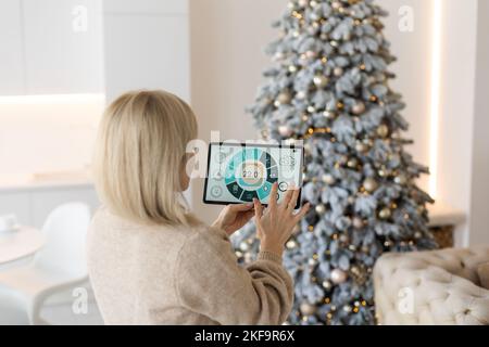 Moderna app di automazione domestica intelligente sul display del tablet nelle mani di una donna a Natale Foto Stock