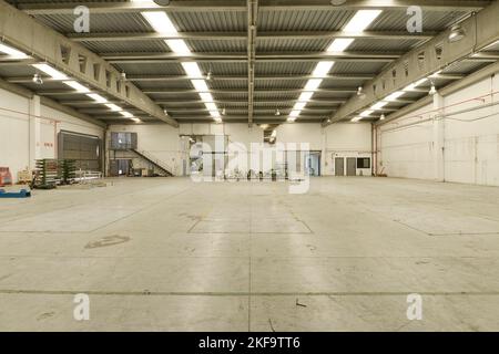 Un grande magazzino industriale vuoto con pavimenti in cemento e lucernari nei soffitti e travi in cemento che li sorreggono Foto Stock