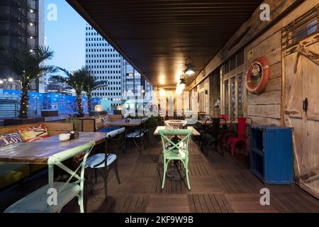 Sala da pranzo sulla terrazza di un bar con pavimenti in legno e tavoli diversi Foto Stock