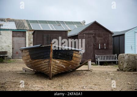 Vecchio scafo marrone barca con rustico vecchio capannone e case fuori sullo sfondo. Panca su cui sedersi. Foto Stock