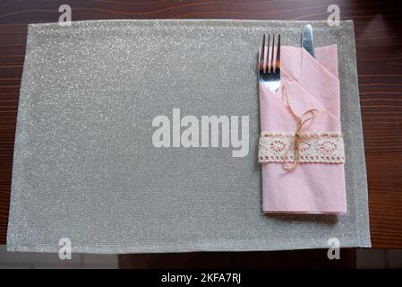 Una vista dall'alto di un panno grigio lucido e argenteria in un tovagliolo rosa su un tavolo di legno. Foto Stock