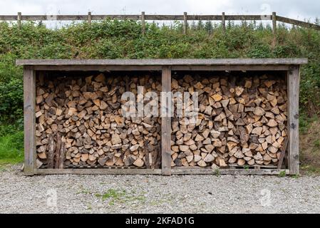 Grande contenitore di stoccaggio in legno con pezzi tagliati di tronchi che asciugano all'interno. Tronchi tagliati di legno per fare combustibile per bruciare in un fuoco di ceppo. Foto Stock