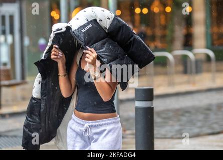 Ragazza che tiene l'anorak DI PLAYBOY sopra la sua testa a Preston, Lancashire. Meteo UK 17 Nov 2022. Tempo umido e ventoso per gli amanti dello shopping nel centro della città. Credit; MediaWorldImages/AlamyLiveNews Foto Stock