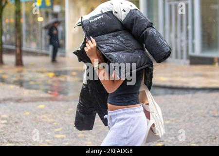 Ragazza che tiene l'anorak DI PLAYBOY sopra la sua testa a Preston, Lancashire. Meteo UK 17 Nov 2022. Tempo umido e ventoso per gli amanti dello shopping nel centro della città. Credit; MediaWorldImages/AlamyLiveNews Foto Stock