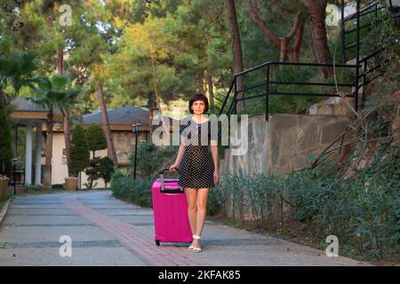 donna con grande valigia rosa brillante è in piedi sulla strada senza sapere dove andare dopo. Foto Stock