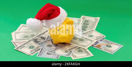 Bonus e spese natalizie. Piggy bank con cappello di Santa sul mucchio di soldi di dollari degli Stati Uniti, sfondo verde. Foto Stock