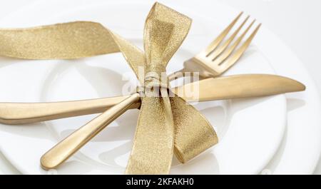 Vista ravvicinata sul tavolo di Natale. Posate dorate e decorazioni su piatti bianchi, elegante ristorante, cena di festa Foto Stock