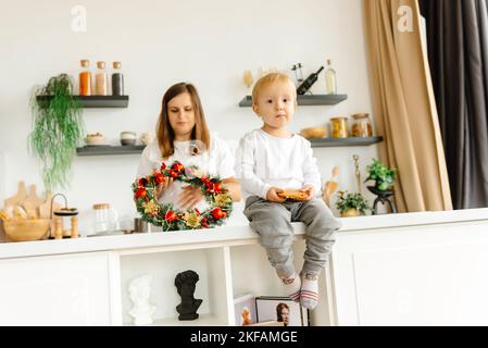 La mamma si sta preparando per Natale e il bambino è seduto accanto al suo mangiare biscotti di farina d'avena Foto Stock