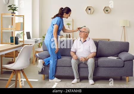 L'infermiera giovane amichevole pettina i capelli dell'uomo anziano che siede sul divano nella casa di cura. Foto Stock