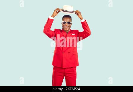Felice uomo afroamericano in abito rosso alla moda e occhiali da sole sorride e indossa il cappello panama Foto Stock