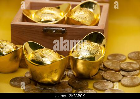 Lingotti e monete d'oro cinesi in cassa del tesoro su sfondo giallo. Concetto di ricchezza e prosperità. Foto Stock